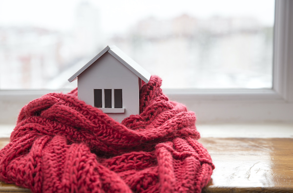 heating system concept and cold snowy weather with model of a house wearing a knitted cap