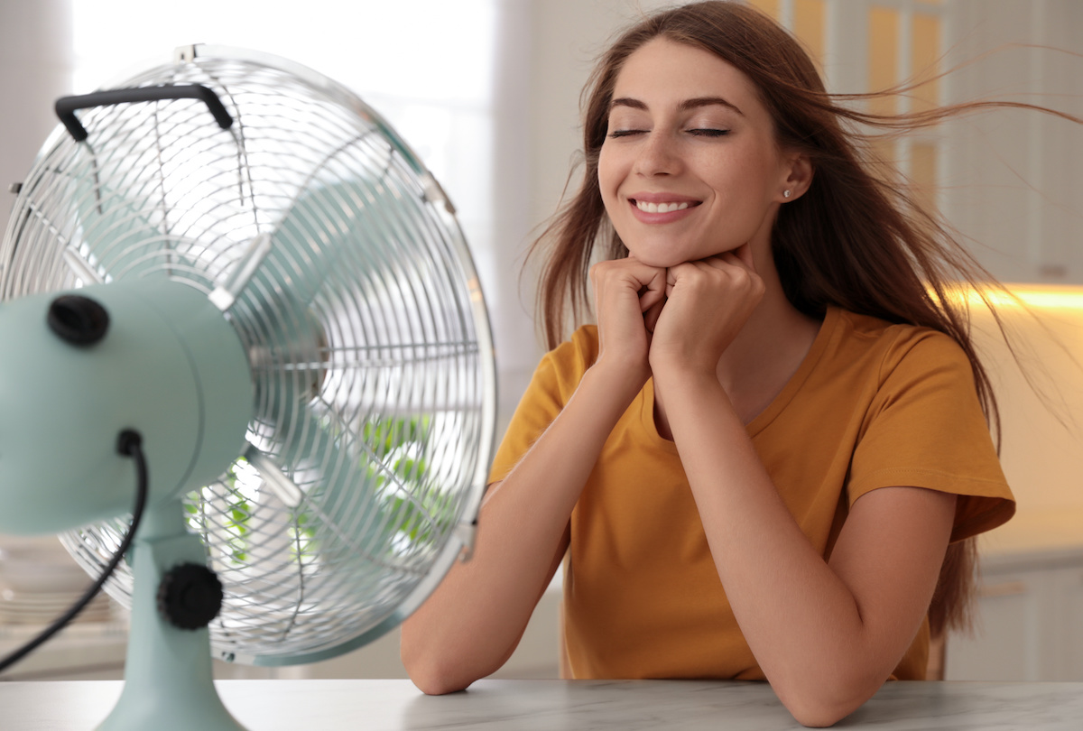 Woman enjoying air flow from fan at table in kitchen. Summer heat