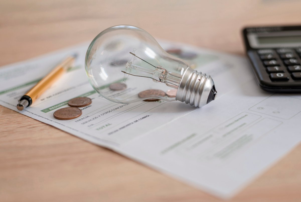 Electricity bill with light bulb, several coins, calculator and pen on the desk. Concept of electricity prices and tax payments